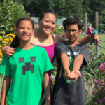 Woman with two youths smiling at camera in a blooming garden.